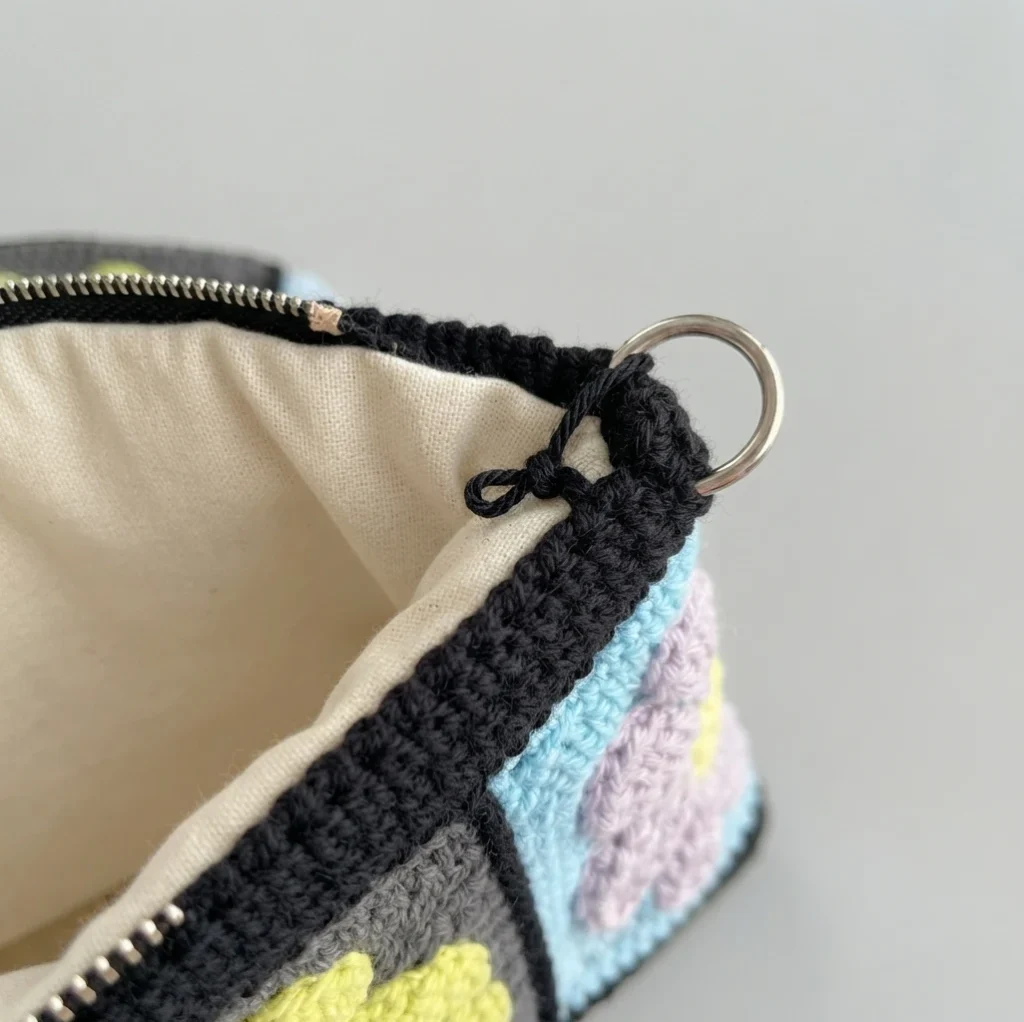 Close-up of crochet granny square bag edge showing cream lining, black crochet border, zipper and metal ring