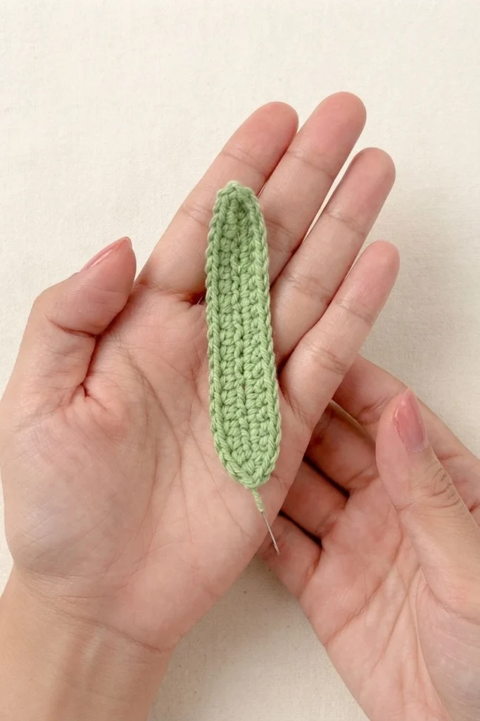 Hands holding a light green crocheted leaf with a fine wire extending from its base
