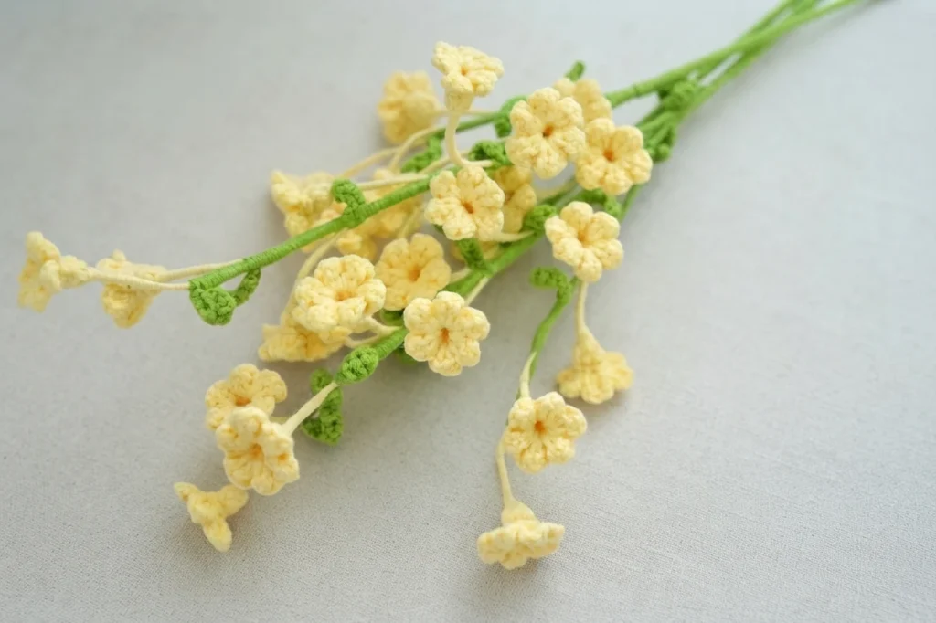 Small pale yellow crochet winter jasmine flowers with green stems laid on a light grey fabric surface