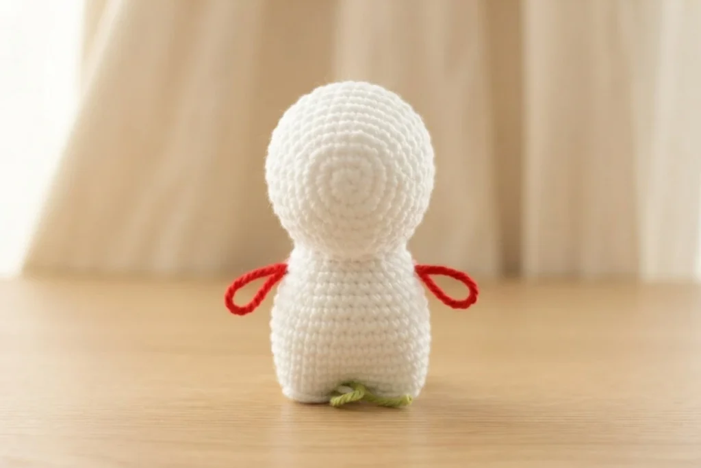 White crochet dinosaur body piece with red stitch markers standing on a wooden table