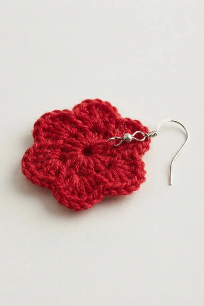 Single red crochet flower earring with a silver hook lying on a plain white background