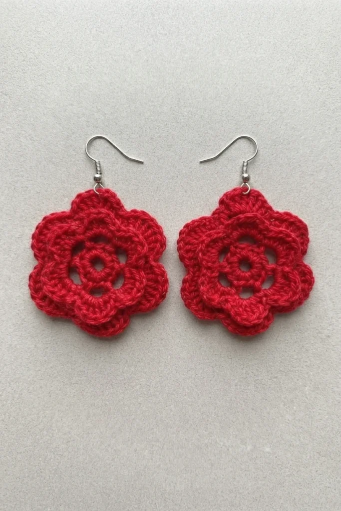 Pair of red crochet flower earrings with layered petals and silver hooks on a light plain background