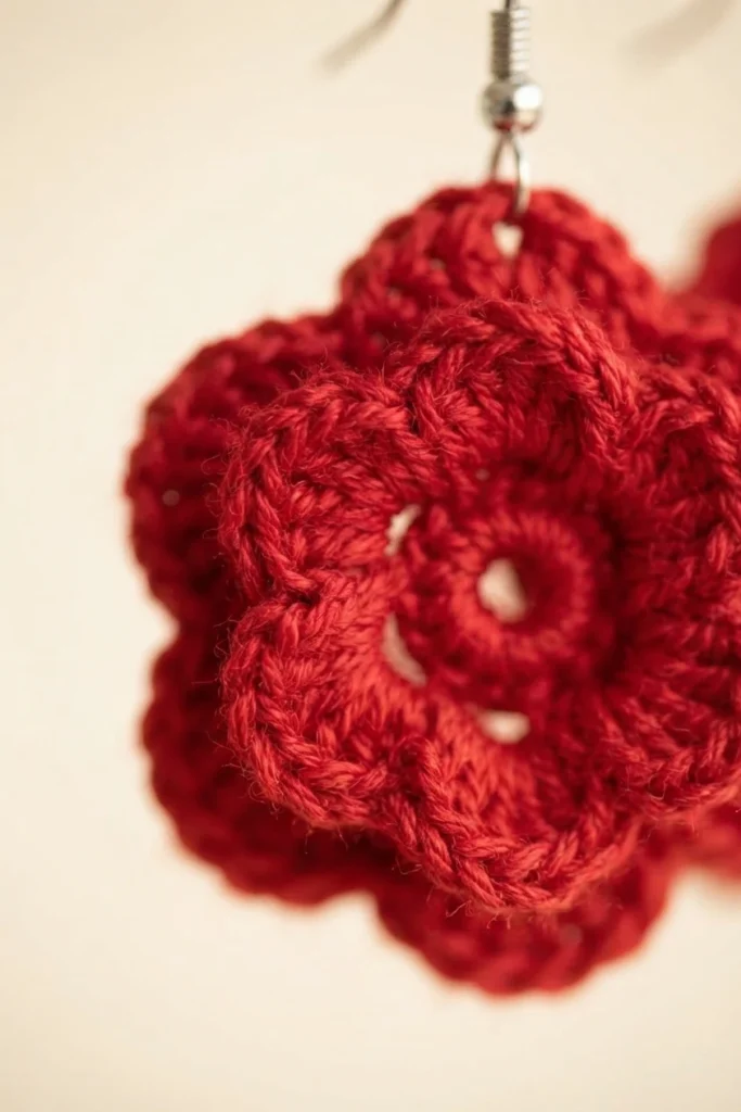 Close up of a red crochet flower earring with a metal earring hook on a plain light background