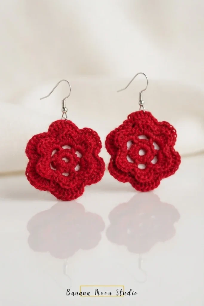 A pair of red layered crochet flower earrings with silver hooks standing on a white reflective surface