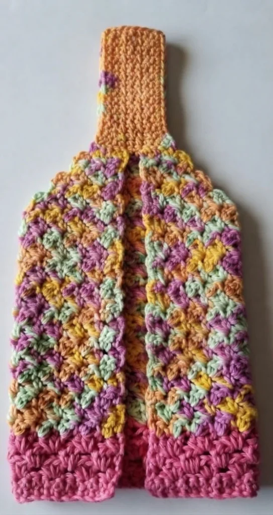 Crocheted hanging towel in variegated pink, green, yellow and orange yarn with a solid pink bottom border and an orange hanger tab, shown folded with a center opening