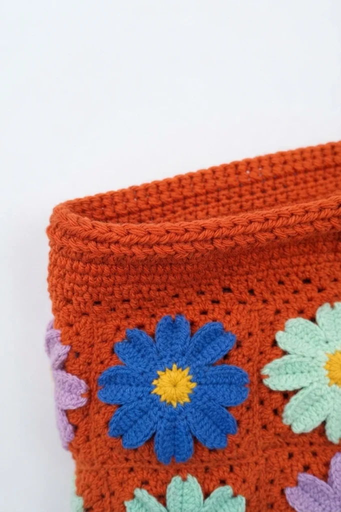 Close-up of terracotta crochet bag opening with solid crochet border above blue and mint daisy motifs