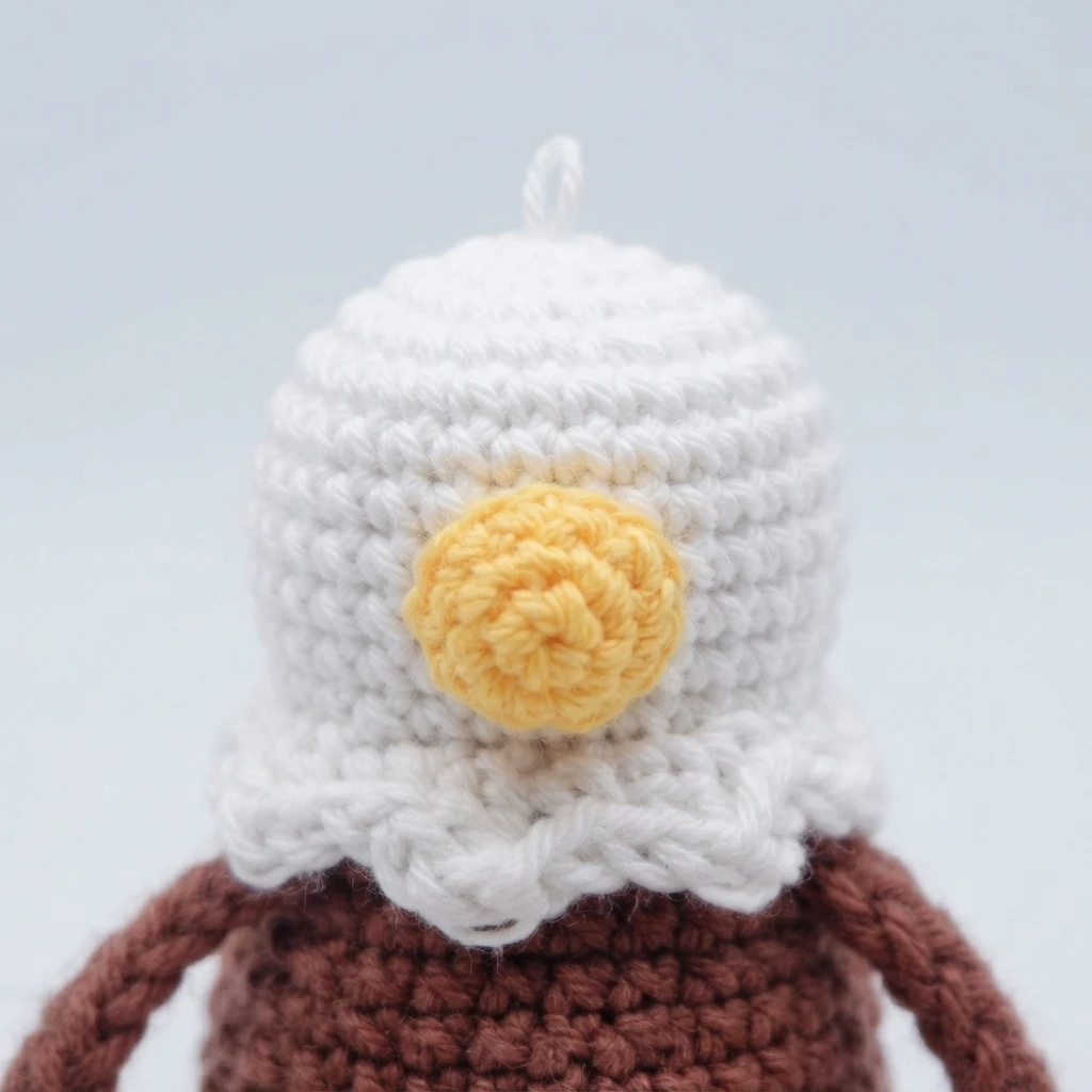 Close-up of a white crocheted eagle head with a round yellow beak, white neck feathers and a brown body below