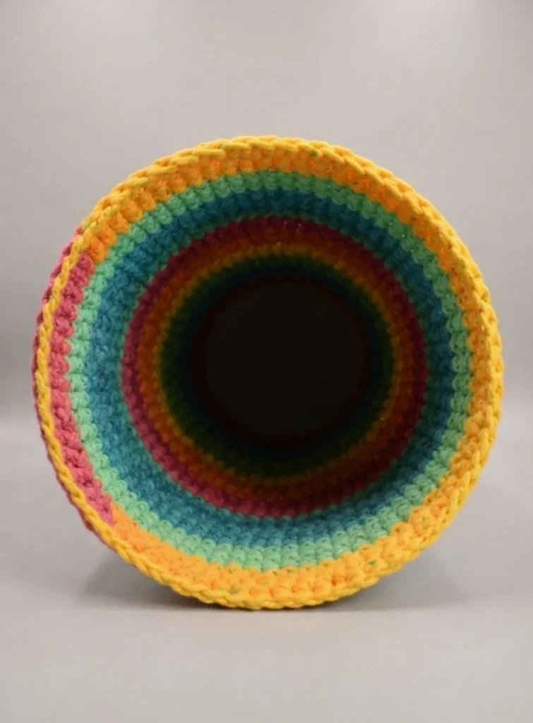 Open end of a colorful striped crochet tunnel in yellow, green, teal and pink yarn.