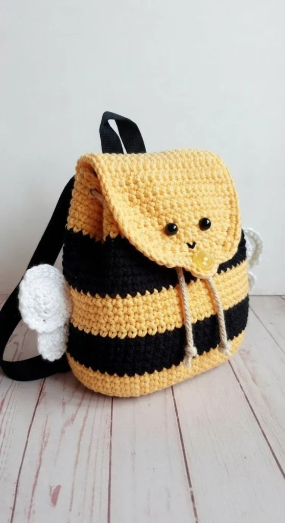Crochet bumble bee backpack with yellow and black stripes, yellow flap with a face and button, white wings and black straps