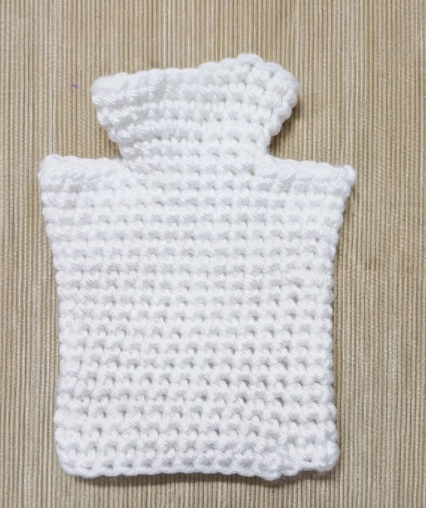 White crocheted ghost hand puppet body in progress, a flat single crochet piece with a narrower head section and open edges, resting on a beige ribbed surface