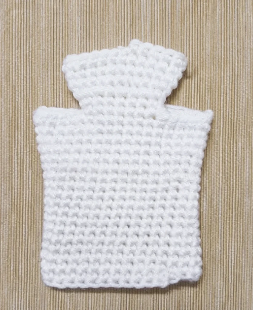 White crocheted ghost puppet body in progress, rectangular with a narrower rounded top, laid flat on a beige ribbed fabric background.