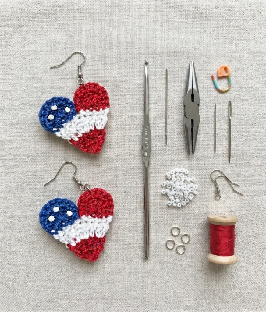 Pair of red, white and blue crochet heart earrings beside a steel crochet hook, flat nose pliers, needles, white seed beads, jump rings and a spool of red thread on linen