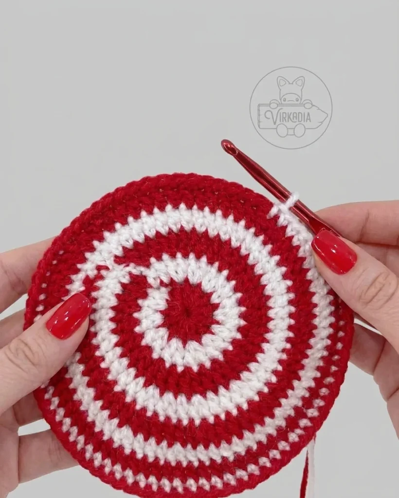 Hands hold a red-and-white crocheted circle with concentric rings and a crochet hook.