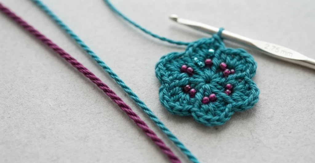 Teal crochet flower motif with pink beads on a 2.75 mm crochet hook beside strands of plum and teal crochet thread.