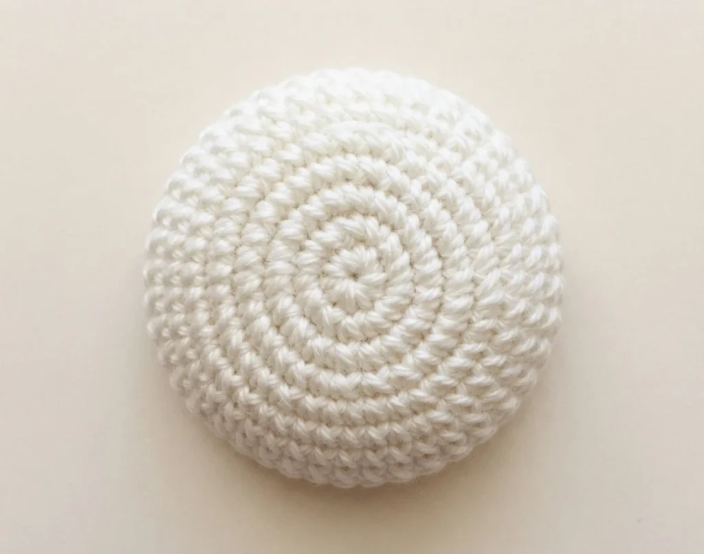 White crocheted flat circular piece worked in rounds for the clown head, shown on a plain cream background