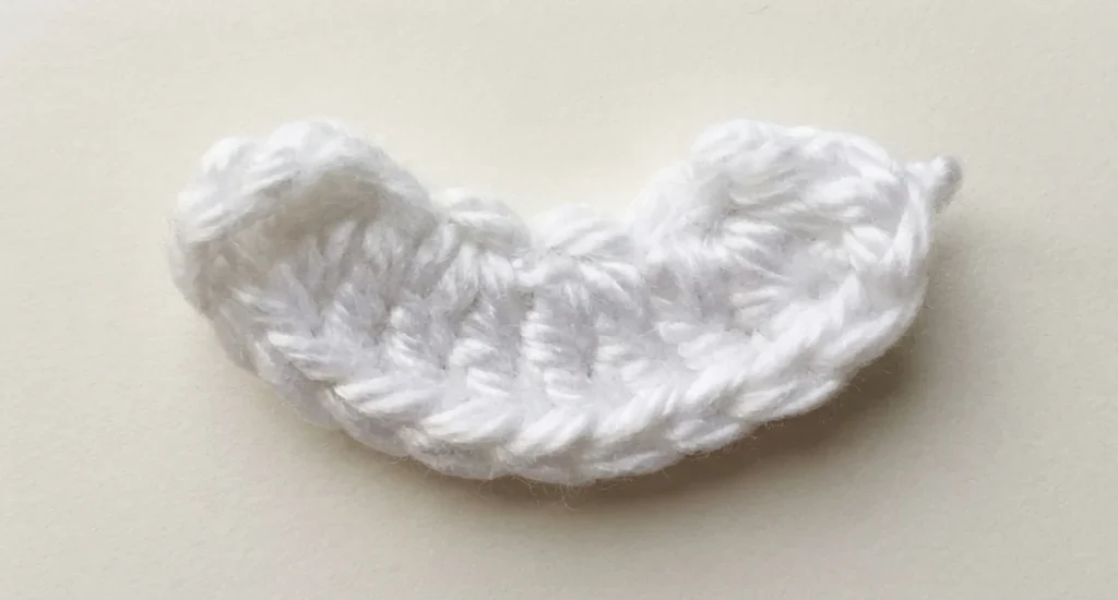 White crocheted mouth piece, a small curved oval component, resting on a plain light beige surface.