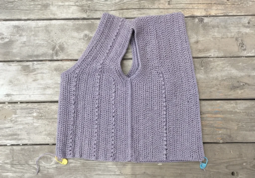 Lavender crocheted summer top with V neckline, bead stitch columns and closed side seams lying flat on wooden planks