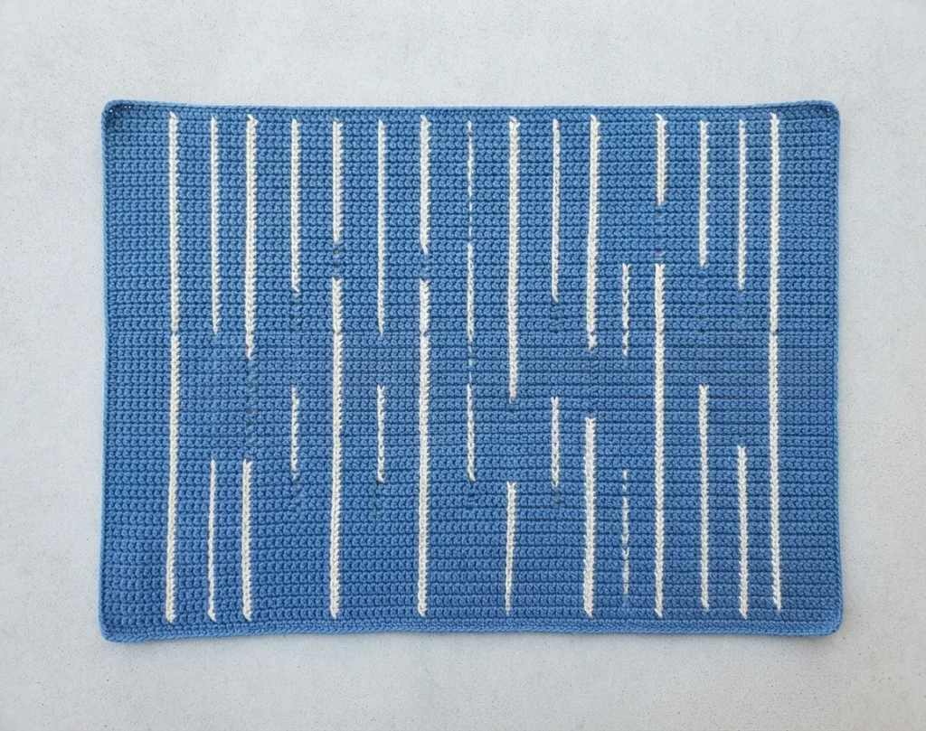 Blue rectangular crochet panel with long white vertical spike stitch lines on a light background