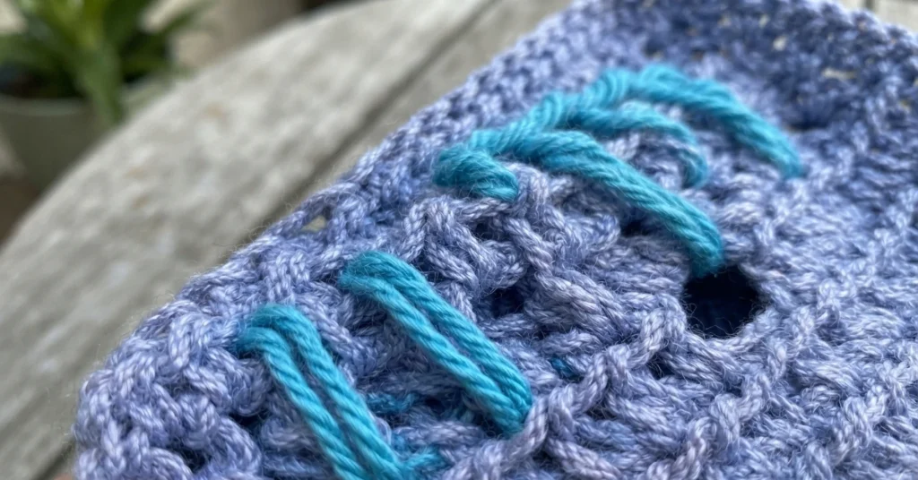 Close-up of lavender crochet fabric with turquoise spike stitches looping down across previous rows