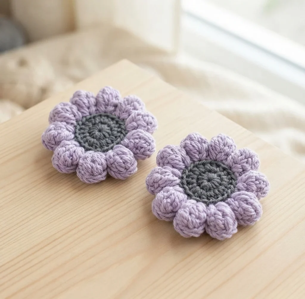 Two crocheted flowers with lilac popcorn petals and grey centers on a wooden surface