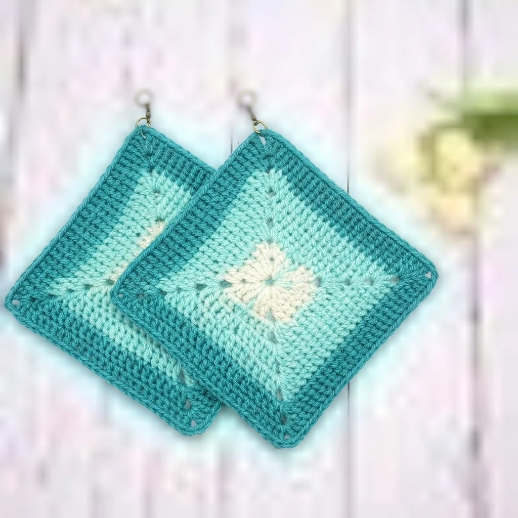 Two crocheted diamond shaped potholders in teal, mint and cream hanging against a light wooden background