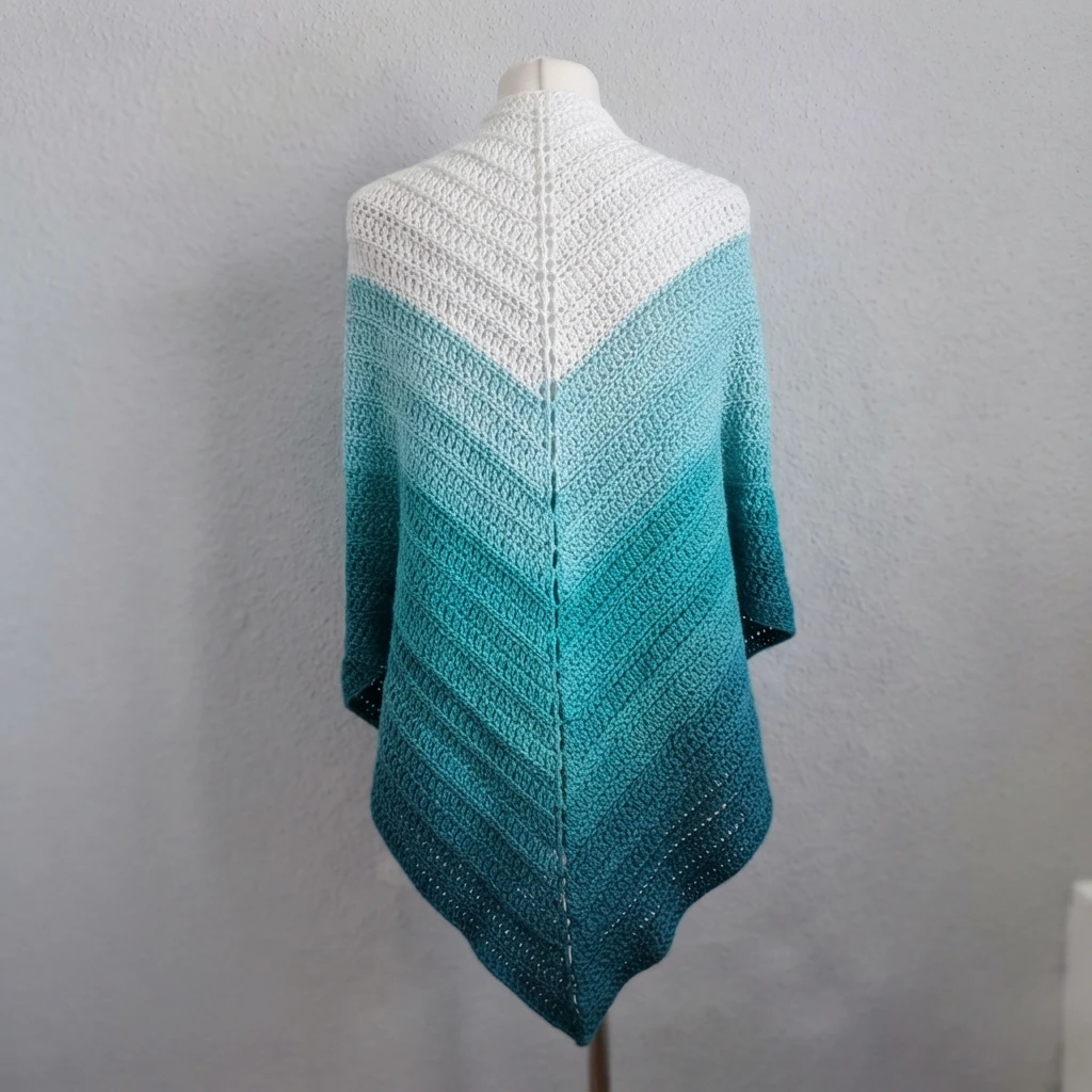 Triangular crochet shawl in white and shades of teal on a dress form against a light wall